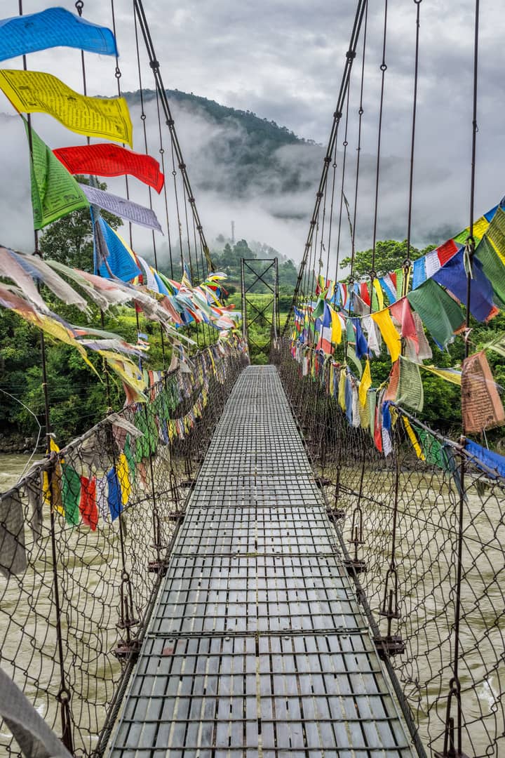 A suspension bridge covered in prayer flags crossing a Bhutanese river