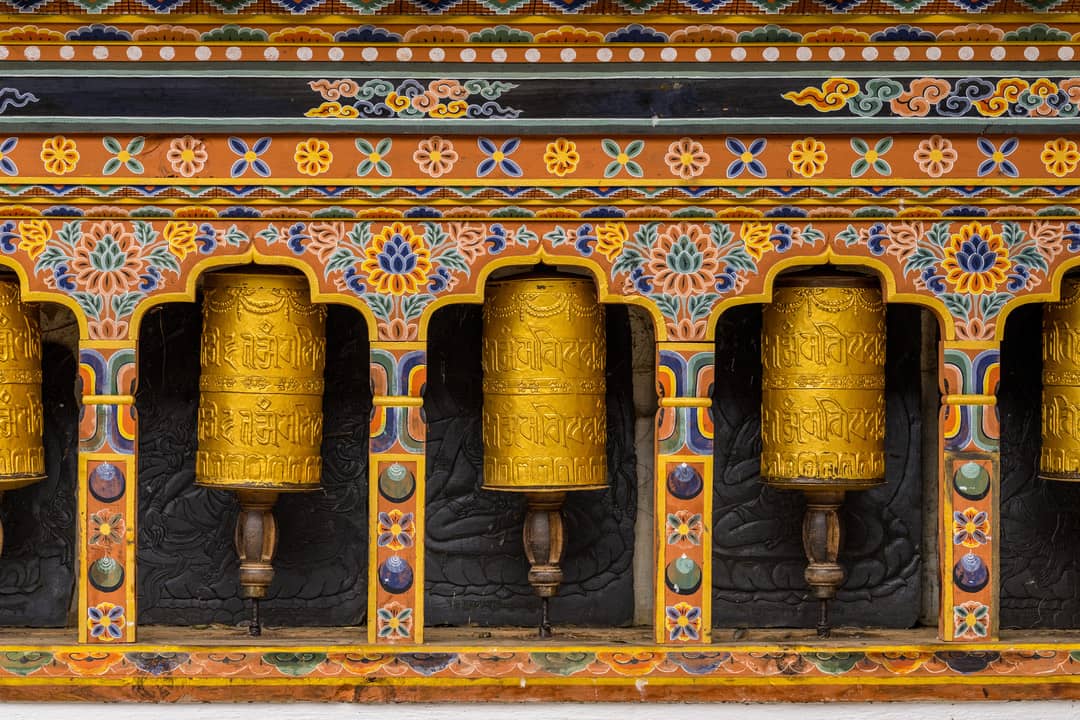 Rows of golden prayer wheels framed by painted Bhutanese patterns
